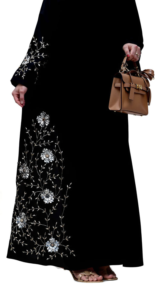 Black abaya with white floral embroidery held by a person with a brown handbag.