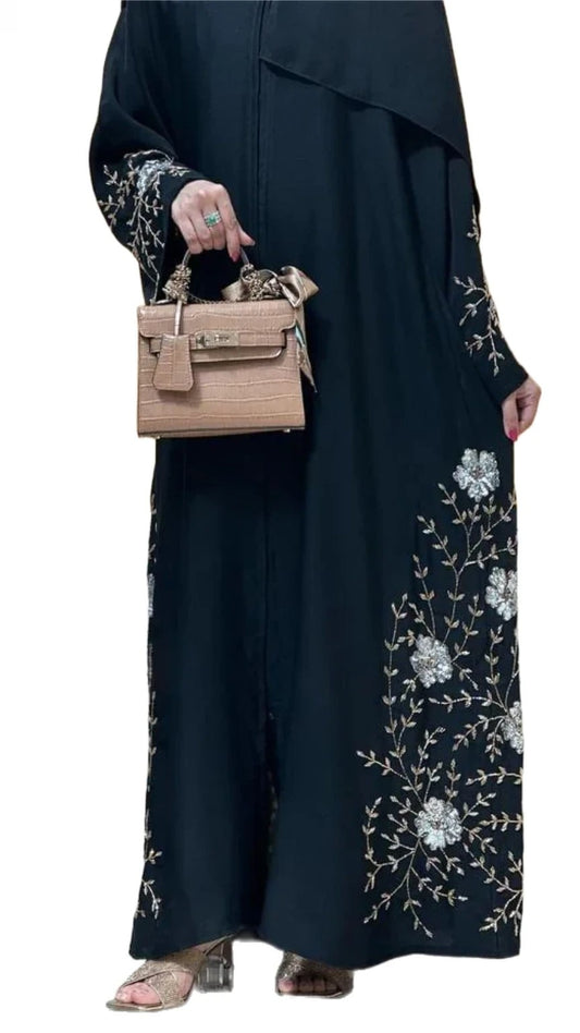 Women wearing a black abaya with floral embroidery, holding a beige handbag on a white background