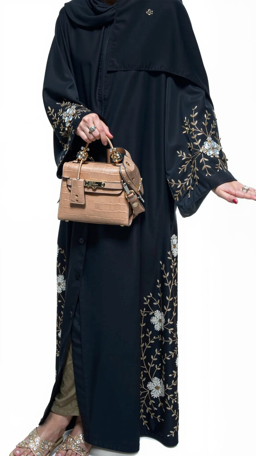 Women wearing a dark abaya with floral embroidery, holding a beige handbag on a white background