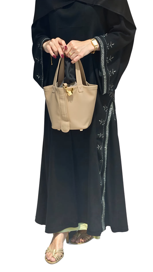 Women wearing a black outfit with white embroidery, holding a beige handbag on a white background