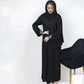 Woman wearing a black abaya standing next to a chair on a white background