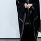 Women wearing a black abaya with intricate patterns on a white background