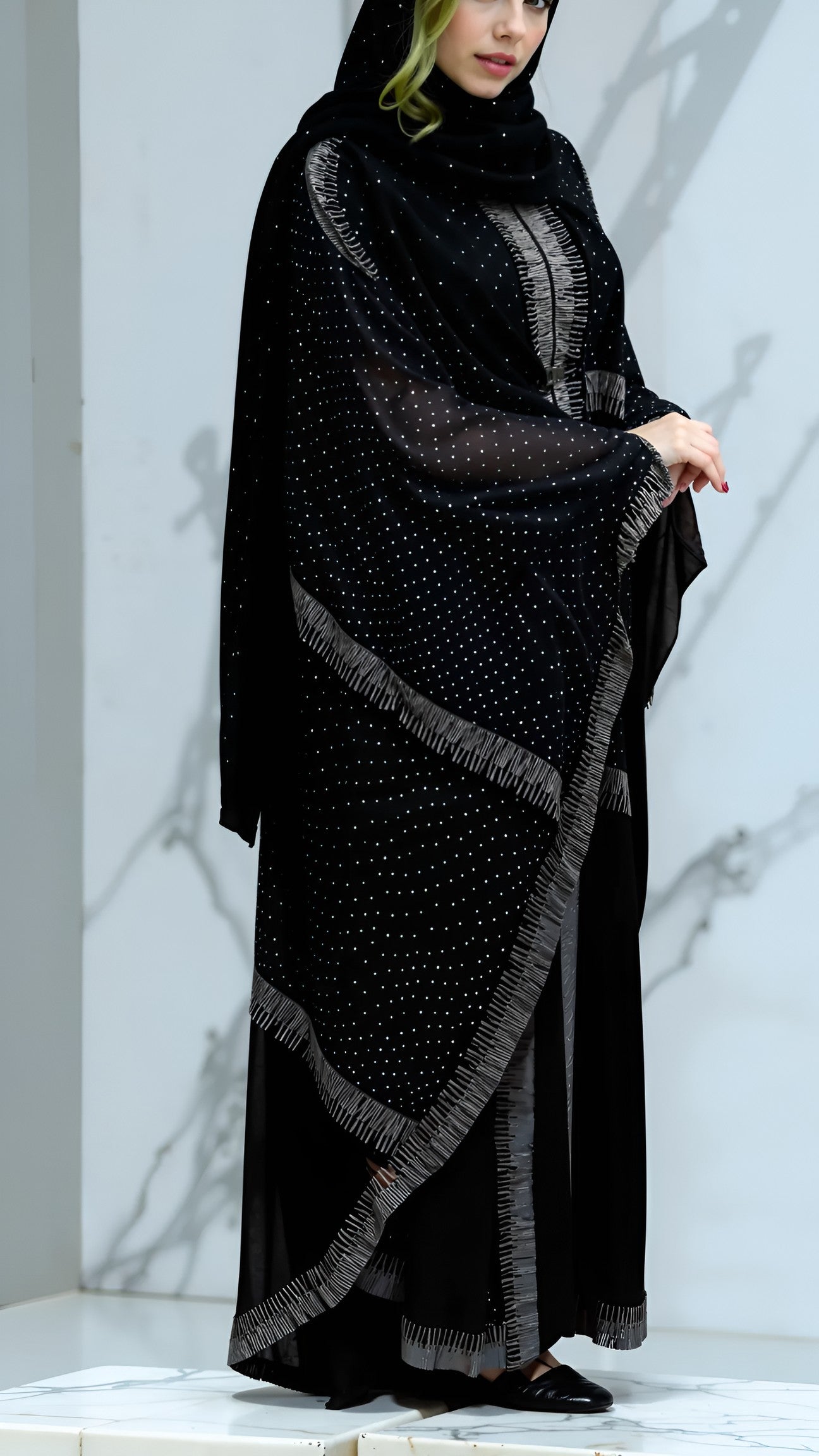 Woman wearing a black abaya with intricate patterns on a marble background