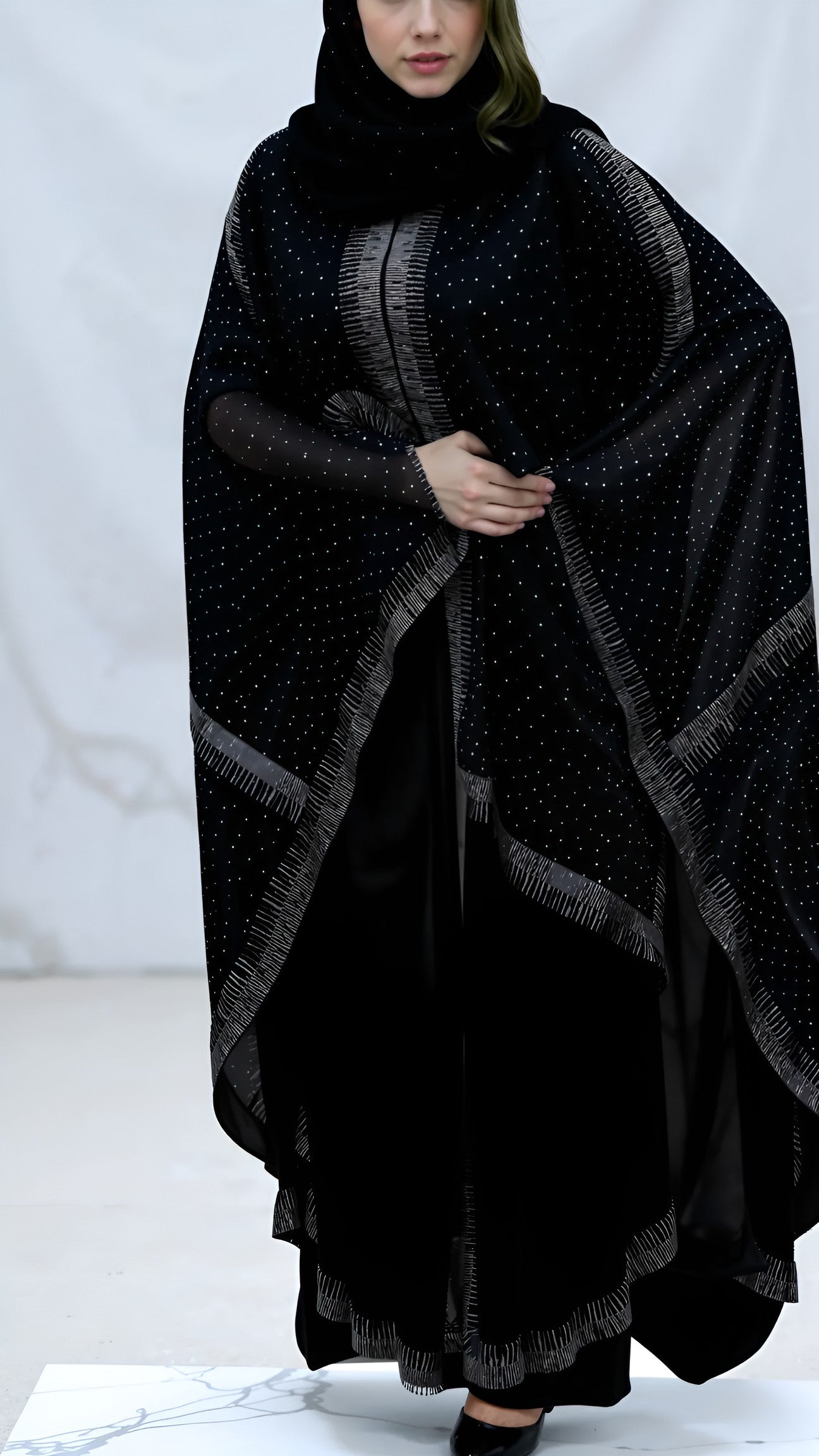 Person wearing a black poncho with a pattern on a white background