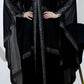 Woman wearing a black abaya with intricate detailing on a white background