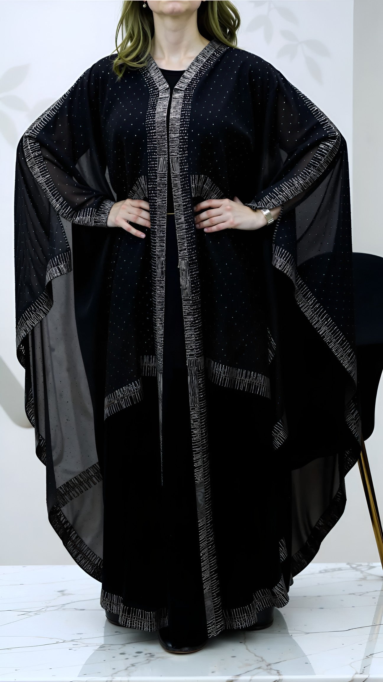 Woman wearing a black abaya with intricate detailing on a white background